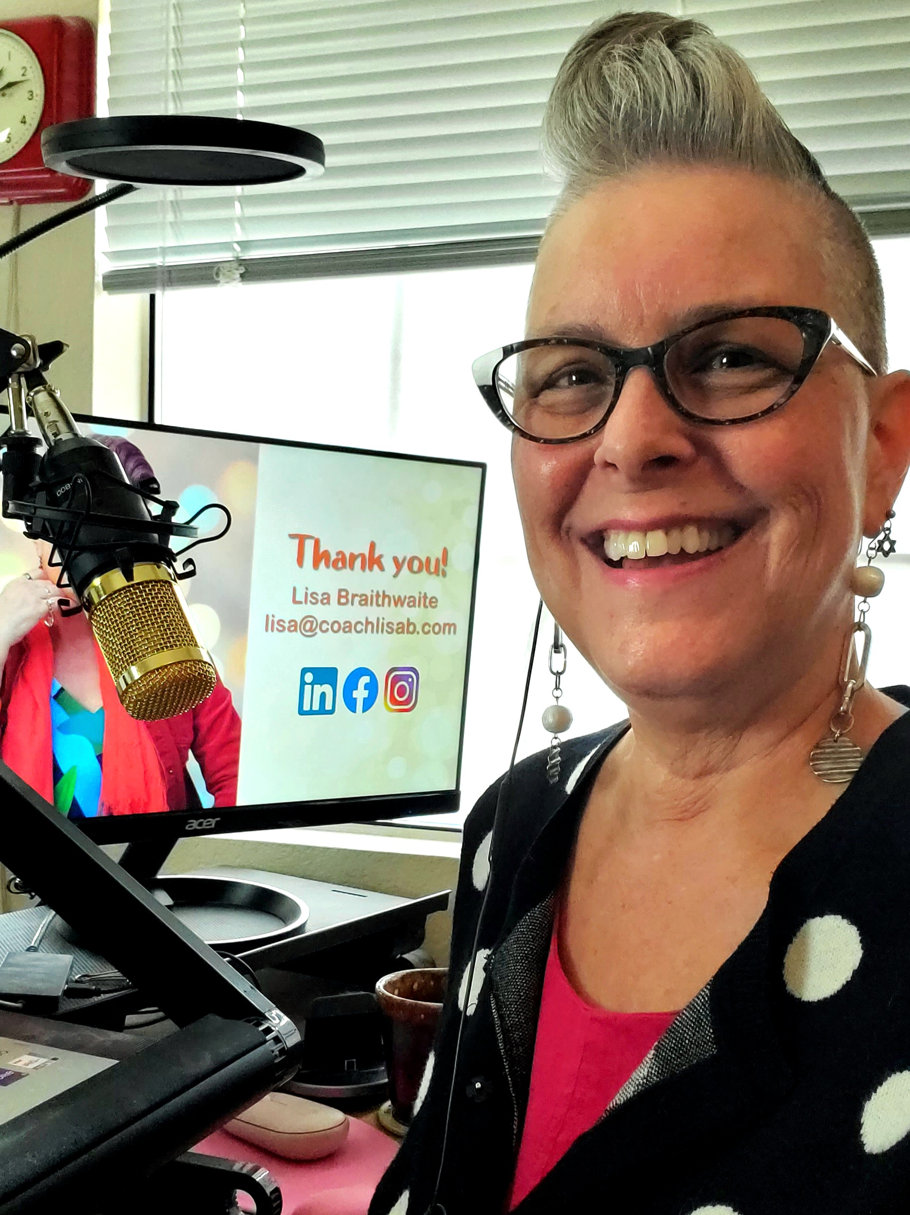 Lisa sitting at her computer at the end of a virtual presentation, wearing a black and white polka dot sweater, her pixie undercut in a quiff, and wearing eyeglasses and dangly earrings.